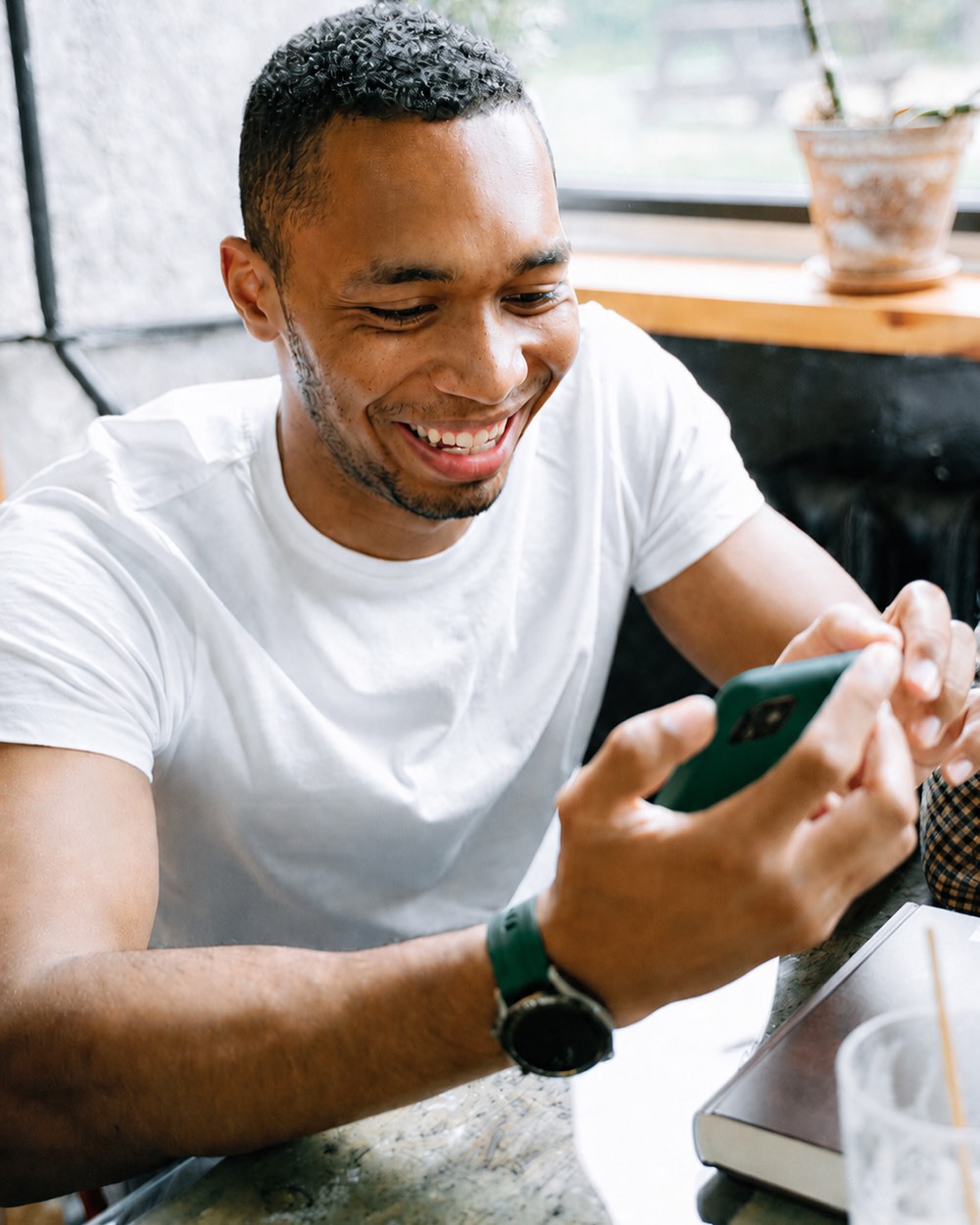 Prestador sorrindo ao receber um pedido pela mPage no celular, sentado em um café.