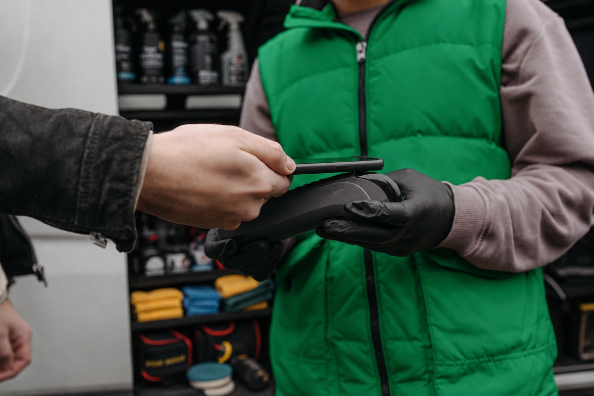 Profissional de estética automotiva de colete verde finalizando um atendimento com um cliente