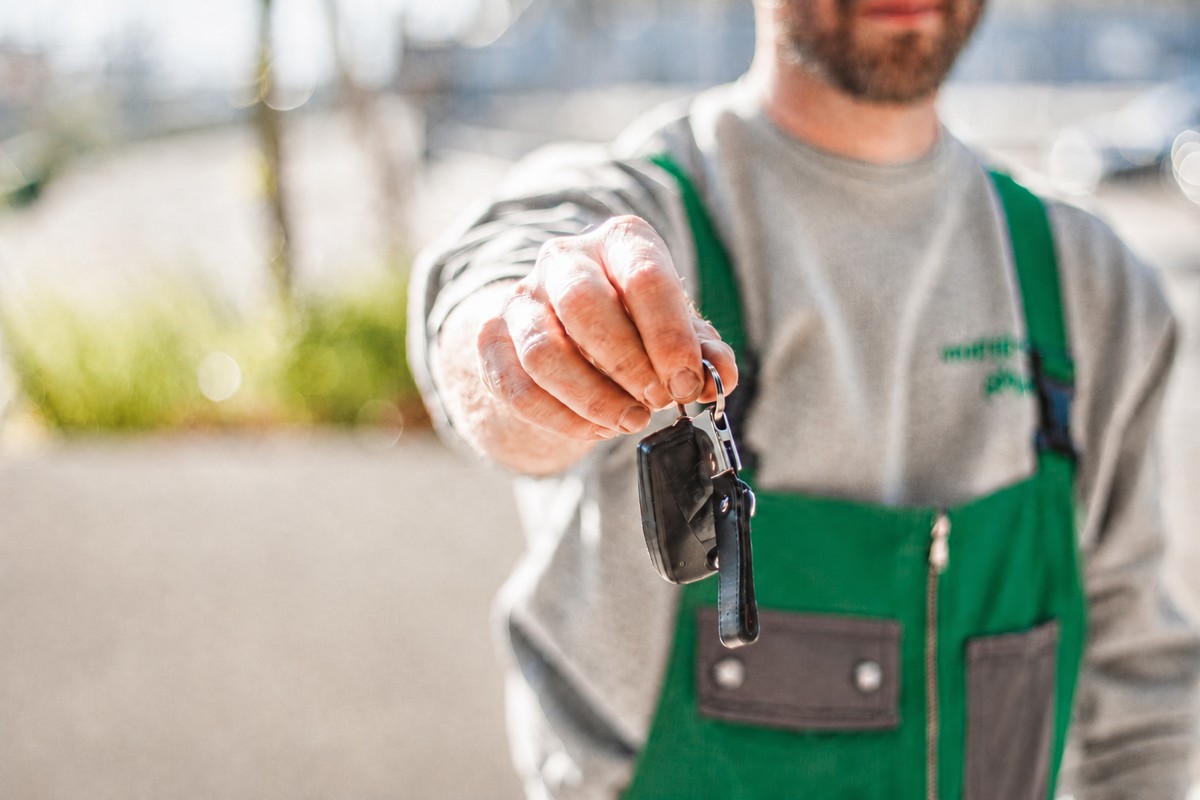Profissional de macacão verde entregando a chave do carro ao cliente
