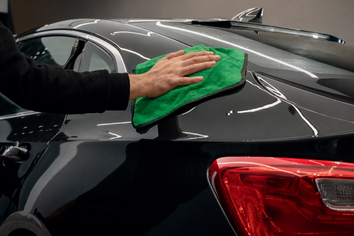 Mão passando uma flanela de microfibra verde na lataria preta e brilhante de um carro